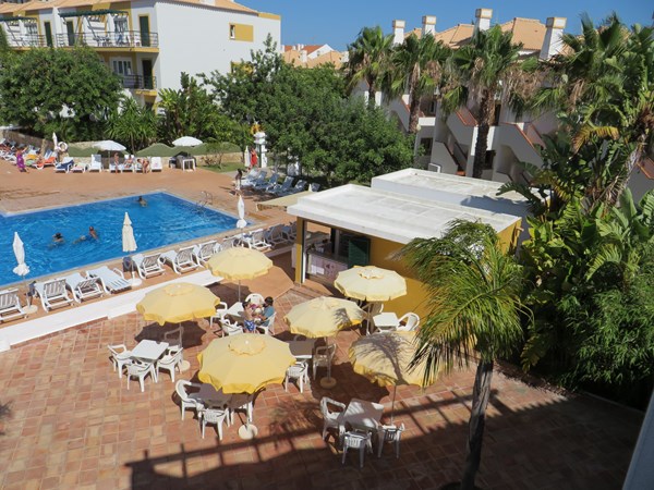 View from apartment towards the pool and pool bar and terrace with tables, chairs and umbrellas